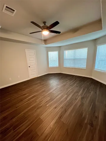 a view of an empty room with wooden floor and a ceiling fan