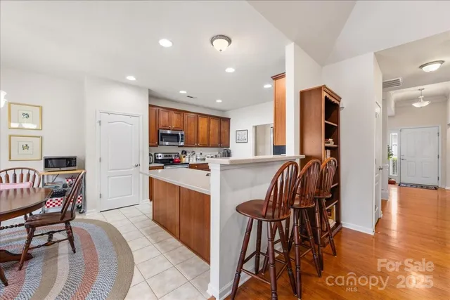 a kitchen with stainless steel appliances granite countertop a refrigerator a stove a sink a dining table and chairs with wooden floor