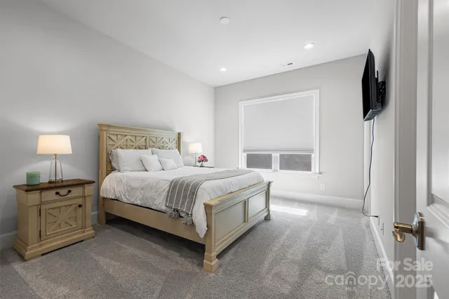 a spacious bedroom with a bed and a flat tv screen on the dresser