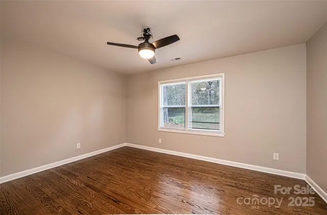 an empty room with wooden floor ceiling fan and windows