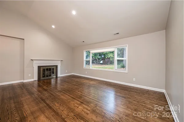 an empty room with wooden floor fireplace and windows
