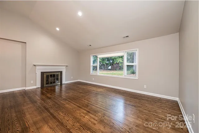 an empty room with wooden floor fireplace and windows