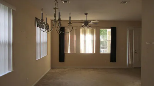 an empty room with chandelier fan and windows