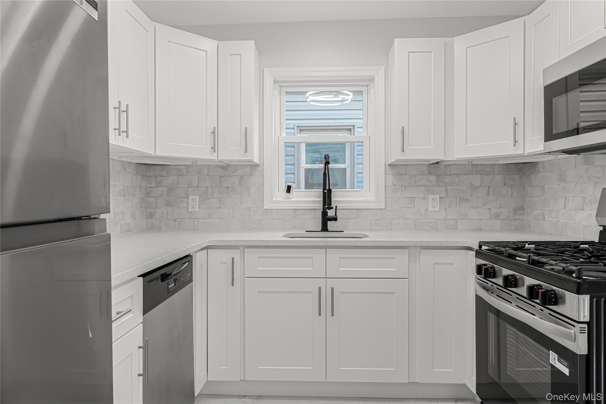 173-43 103rd Road Queens, NY 11433 - Photo 3 of 43 White shaker-style cabinetry with silver hardware, light-toned countertops, white subway tile backsplash, stainless steel gas range, and built-in microwave