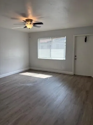 an empty room with wooden floor chandelier fan and windows