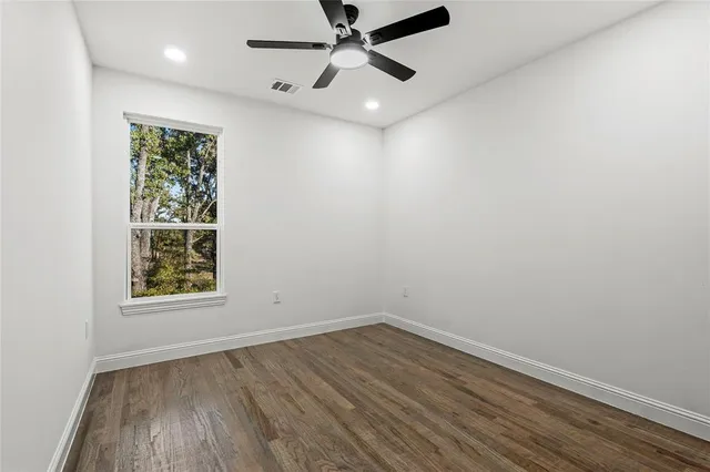 an empty room with wooden floor ceiling fan and windows