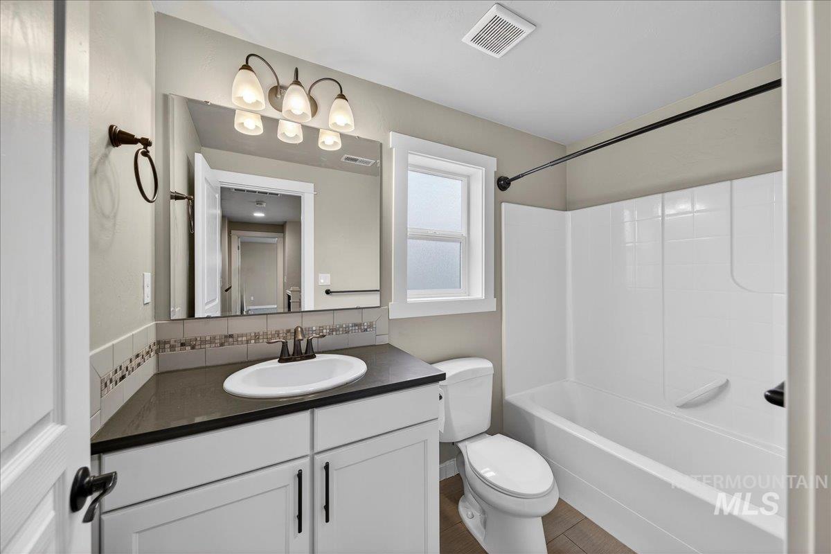 12200 West Oneida Street Boise, ID 83709 - Photo 19 of 35 Full bathroom featuring vanity, shower / bathtub combination, decorative backsplash, and dark wood-style floors