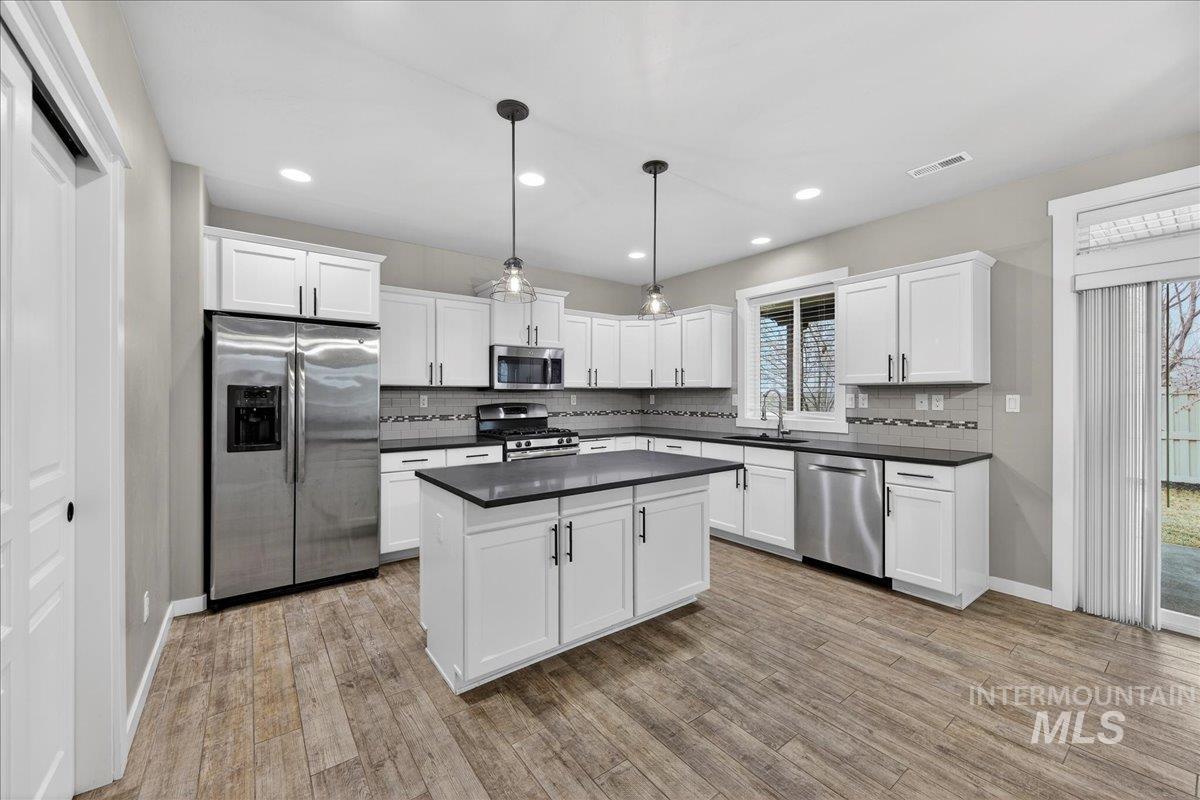 12200 West Oneida Street Boise, ID 83709 - Photo 4 of 35 Kitchen with stainless steel appliances, decorative light fixtures, white cabinets, decorative backsplash, and recessed lighting