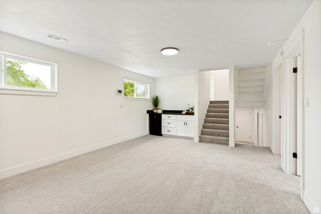 62 South Clark Lane Elk Ridge, UT 84651 - Photo 18 of 30 Spacious flex/family room with dry bar featuring light-colored carpeting, two windows providing natural illumination, and a built-in wet bar with white cabinetry and a dark countertop. Room with fireplace.