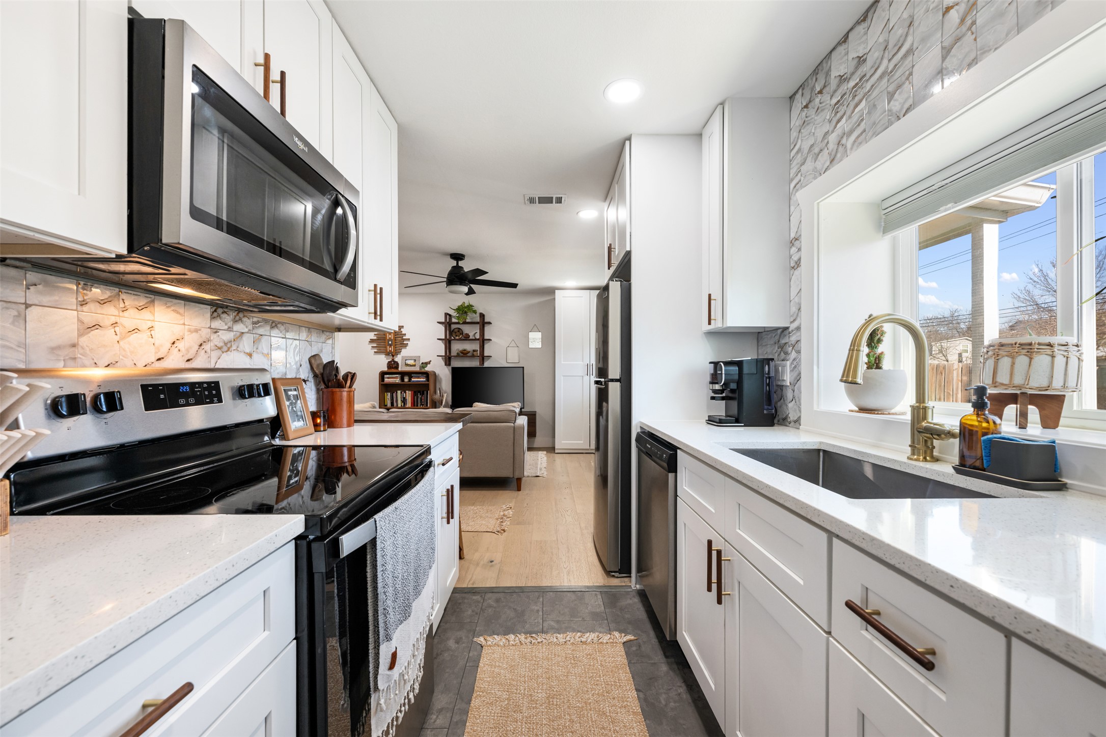 1616 Webberville Road, Unit A Austin, TX 78721 - Photo 20 of 28 Kitchen featuring appliances with stainless steel finishes, ceiling fan, white cabinets, light stone countertops, and decorative backsplash