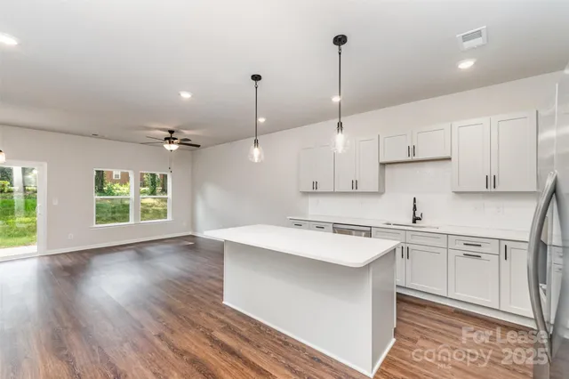 a kitchen with stainless steel appliances granite countertop a sink a stove a refrigerator and white cabinets with wooden floor