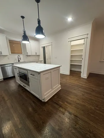 a kitchen with kitchen island a stove a sink a refrigerator white cabinets and wooden floor