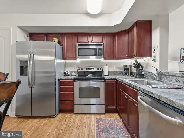 a kitchen with stainless steel appliances granite countertop a refrigerator a stove and a sink with wooden cabinets