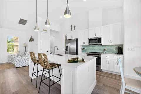 a kitchen with stainless steel appliances granite countertop a refrigerator a sink a stove and white cabinets with wooden floor