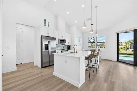 a large white kitchen with a large window a sink stainless steel appliances and cabinets