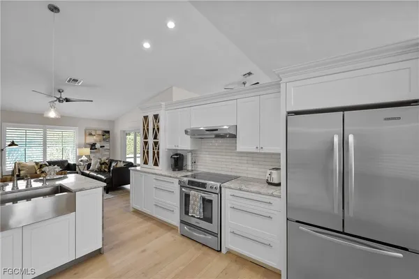 a large kitchen with stainless steel appliances granite countertop a refrigerator a stove a sink dishwasher and white cabinets with wooden floor