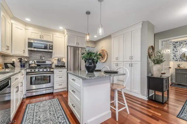 a kitchen with stainless steel appliances kitchen island granite countertop a stove top oven a refrigerator a sink dishwasher and a dining table with wooden floor