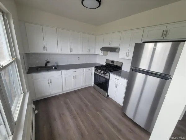 a kitchen with granite countertop a refrigerator a sink and white cabinets