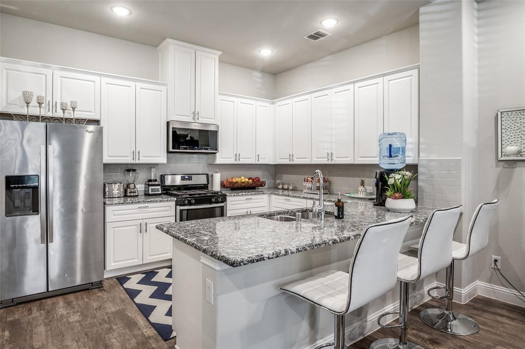 1560 Windermere Way Dallas, TX 75234 - Photo 9 of 25 Kitchen with stainless steel appliances, white cabinetry, a breakfast bar, light stone countertops, and dark wood-style flooring
