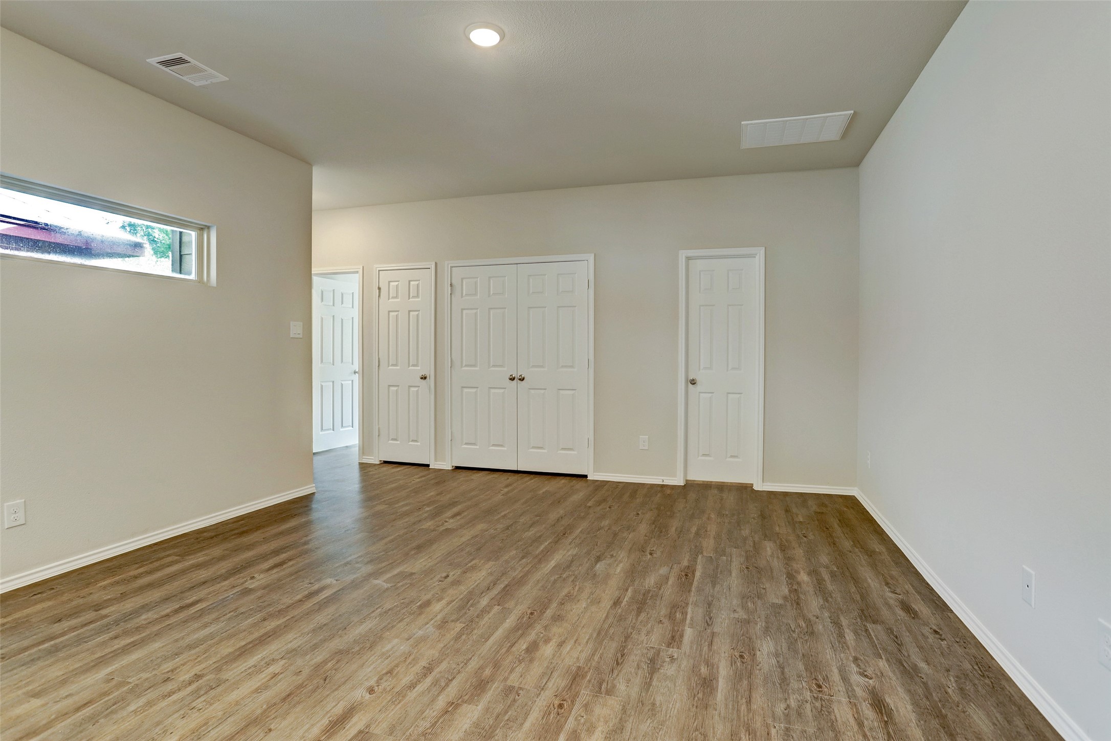 409 South 12th Street, Unit B Conroe, TX 77301 - Photo 8 of 14 This room features a clean, modern design with light wood flooring, neutral walls, and ample natural light from a high window. It includes multiple white doors, likely for closets or additional rooms, creating a functional and versatile space.