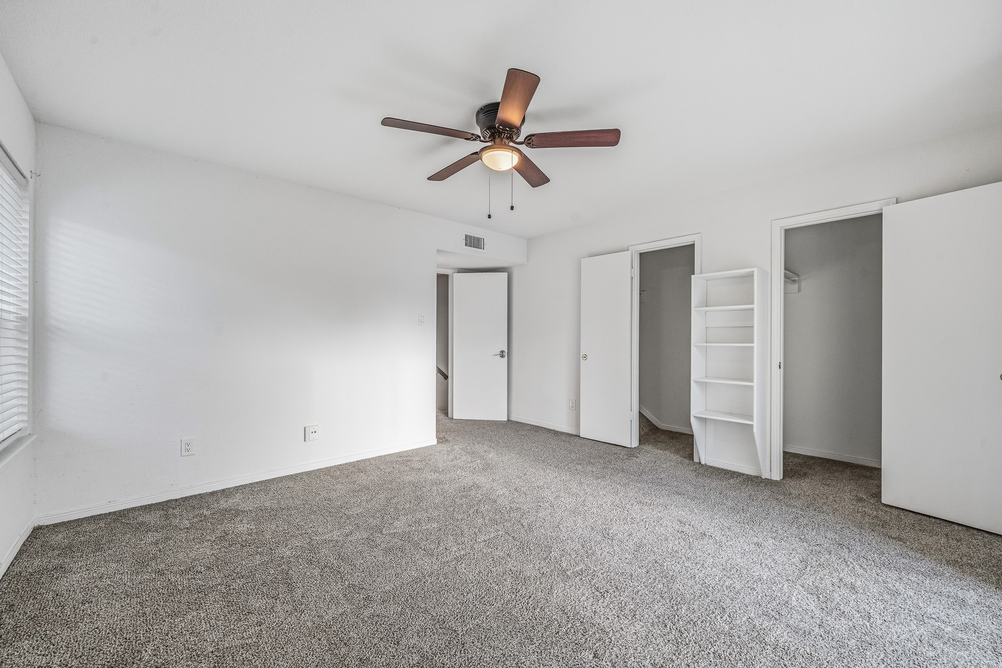830 Threadneedle Street, Unit 240 Houston, TX 77079 - Photo 23 of 33 This spacious bedroom features neutral carpeting, a ceiling fan, and ample natural light. It includes two closets for storage and a built-in shelving unit, with clean white walls for a bright, open feel.