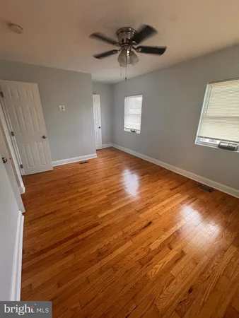 an empty room with wooden floor chandelier fan and windows