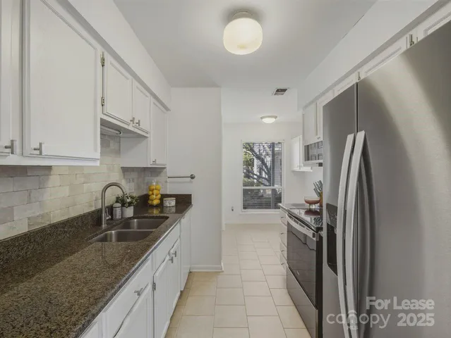 a kitchen with stainless steel appliances granite countertop a refrigerator a sink and white cabinets