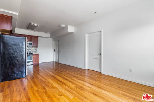 a view of empty room with wooden floor and kitchen