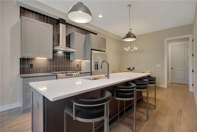 a kitchen with stainless steel appliances a sink a stove a refrigerator and chairs