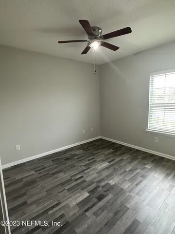 an empty room with wooden floor fan and windows