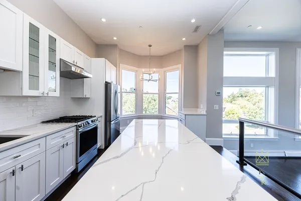 a large kitchen with stainless steel appliances granite countertop a stove a sink and a large window with wooden floor