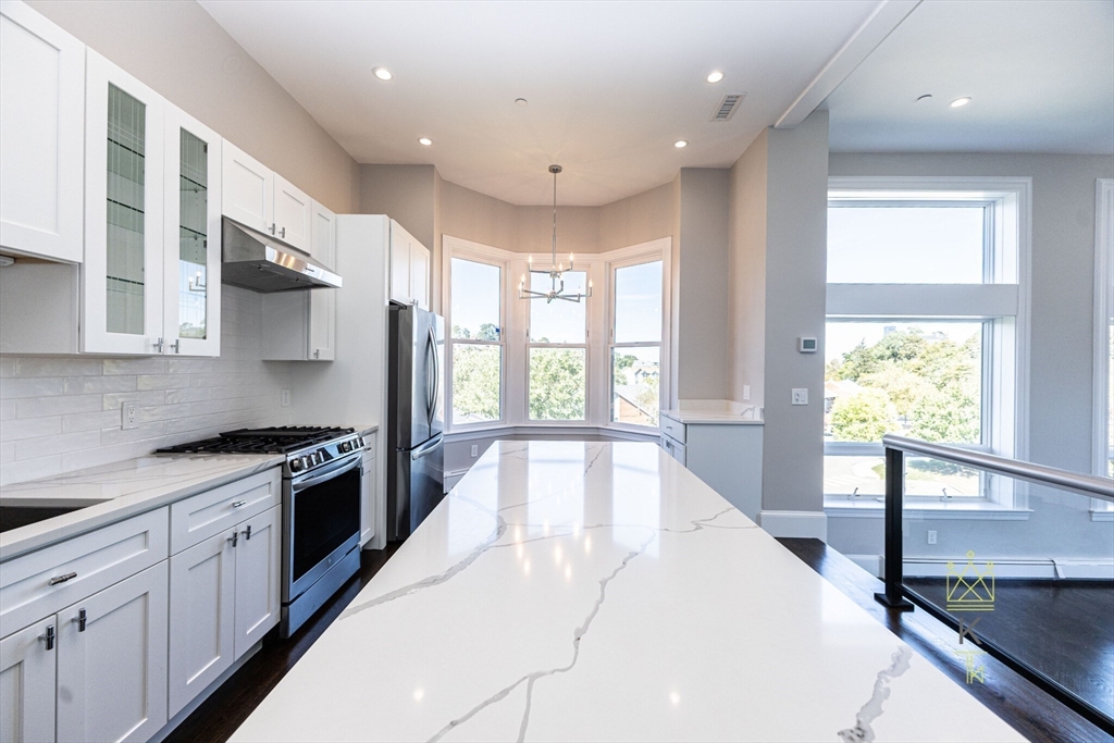 85 Regent Street, Unit 7 Boston, MA 02119 - Photo 4 of 22 a large kitchen with stainless steel appliances granite countertop a stove a sink and a large window with wooden floor