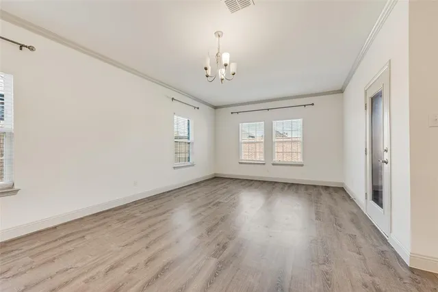 an empty room with wooden floor chandelier and windows