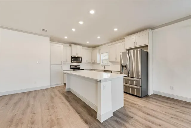 a kitchen with stainless steel appliances kitchen island granite countertop a refrigerator oven a sink and dishwasher with wooden floor