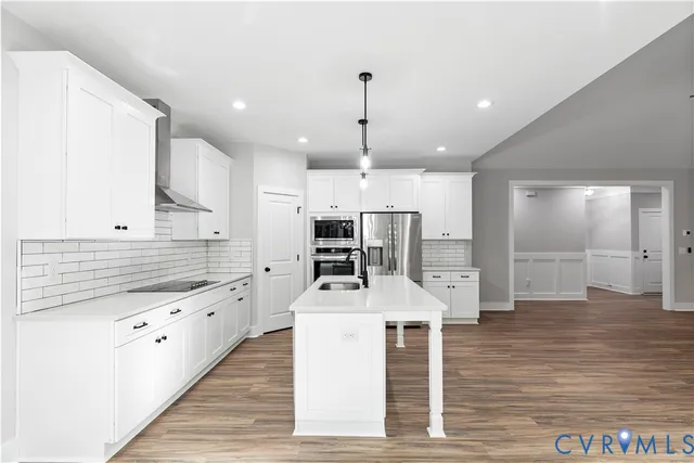 a large kitchen with stainless steel appliances kitchen island granite countertop a stove a sink a refrigerator and white cabinets with wooden floor