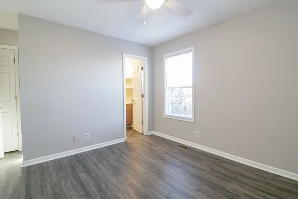 an empty room with wooden floor chandelier fan and windows
