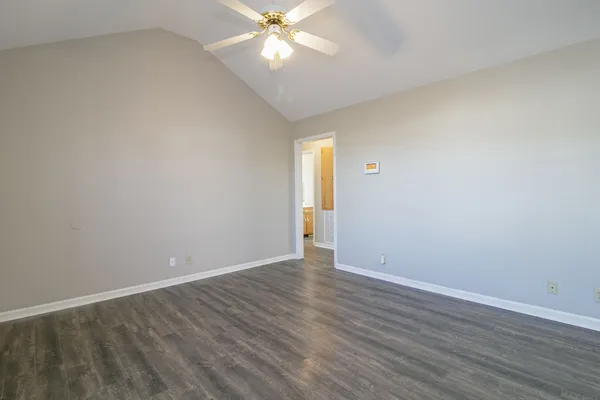 a view of an empty room with wooden floor and a ceiling fan
