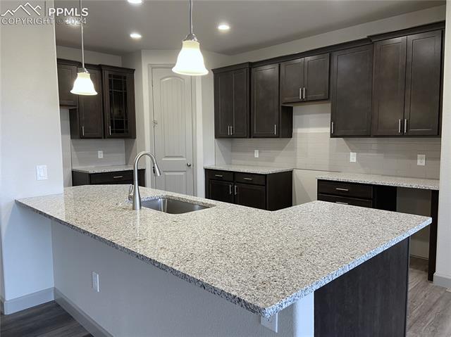 9083 Peaceful Valley Road Colorado Springs, CO 80925 - Photo 6 of 22 Kitchen featuring light stone countertops, tasteful backsplash, wood-type flooring, hanging light fixtures, and sink
