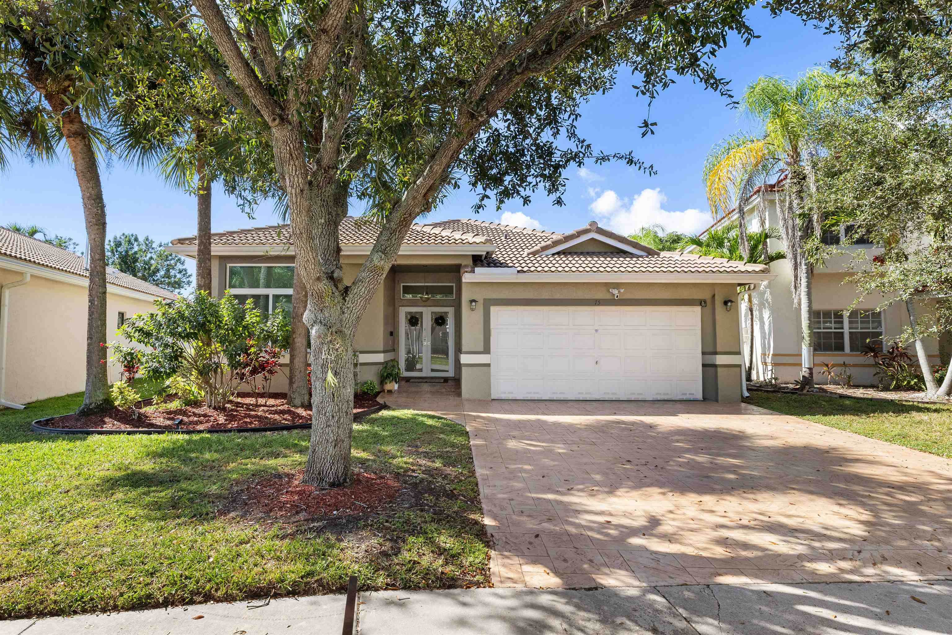 View of front of house featuring decorative driveway, stucco siding, a front lawn, a tile roof, and french doors