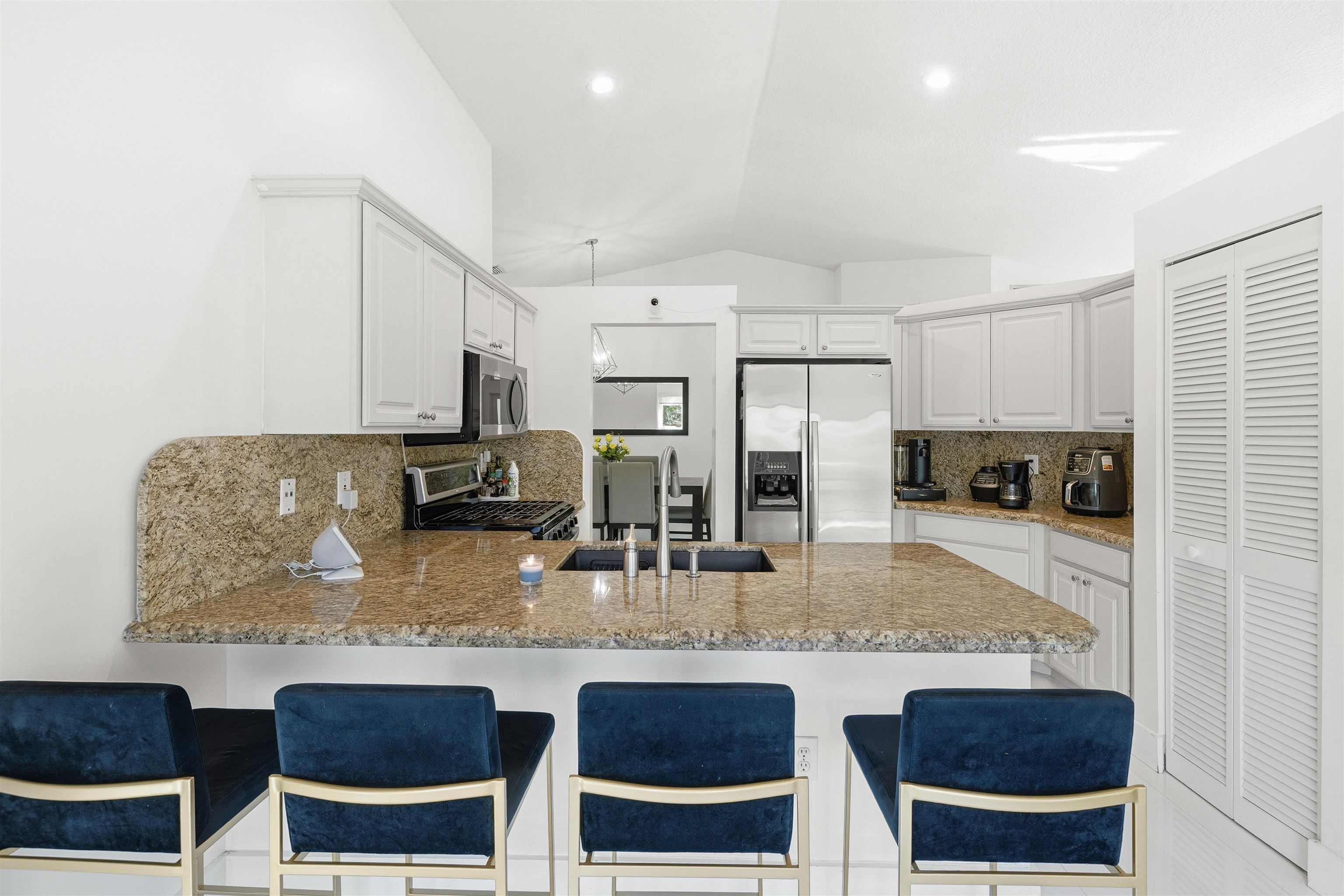 75 Gables Boulevard Weston, FL 33326 - Photo 9 of 29 Kitchen with tasteful backsplash, a peninsula, appliances with stainless steel finishes, vaulted ceiling, and light stone counters