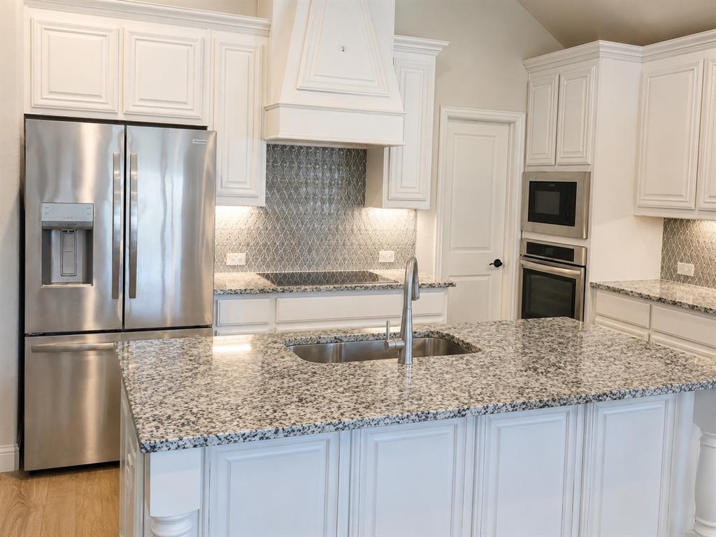 5225 Rowlan Row Midlothian, TX 76065 - Photo 6 of 9 White cabinetry, stainless steel appliances, speckled countertops, kitchen island with sink, and a decorative tile backsplash
