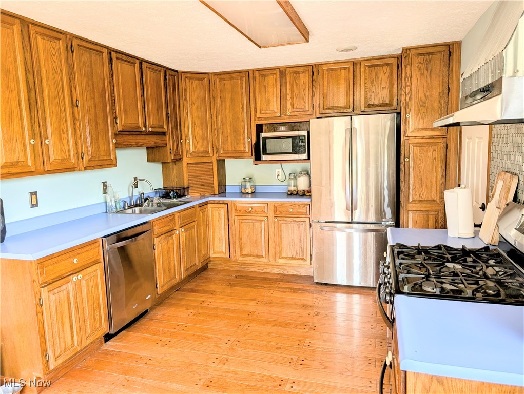 77 Morgan Ridge Road Walker, WV 26180 - Photo 13 of 30 Kitchen with appliances with stainless steel finishes, under cabinet range hood, light wood-type flooring, light countertops, and brown cabinetry