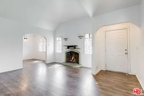 an empty room with wooden floor fireplace and windows
