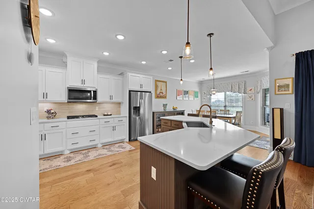 a kitchen with stainless steel appliances kitchen island granite countertop a refrigerator a stove a sink a dining table and chairs with wooden floor