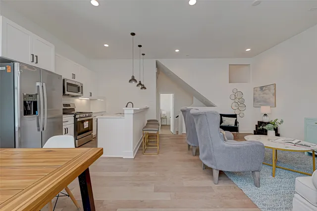 a living room with stainless steel appliances furniture a rug and a kitchen view