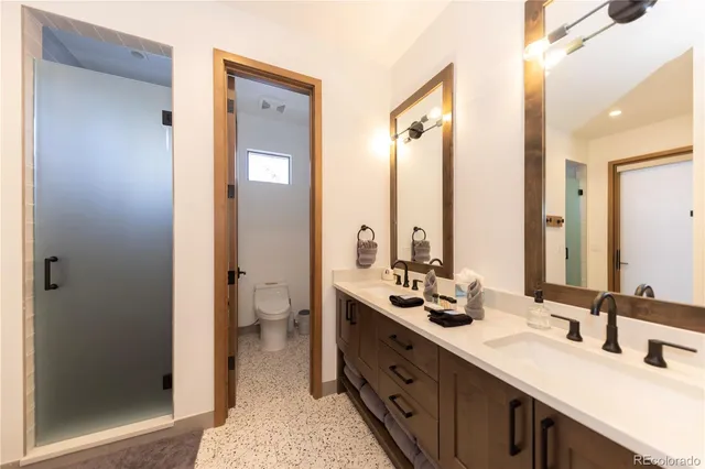 a bathroom with double vanity sinks a toilet a mirror and a shower
