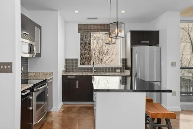 a kitchen with stainless steel appliances granite countertop a refrigerator a stove and a sink with wooden floor