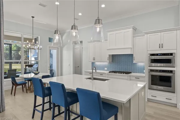 a open kitchen with stainless steel appliances granite countertop a stove a refrigerator a kitchen island a sink white cabinets and couches with wooden floor