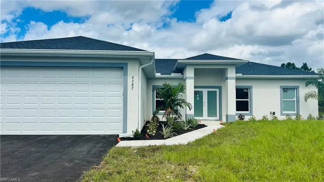 a view of a house with small yard plants and a large tree