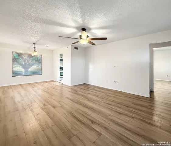 an empty room with wooden floor chandelier fan and windows